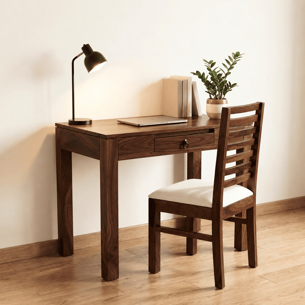 A dark brown wooden writing desk with a matching wooden chair featuring a white cushion, styled in a minimalist room with a black desk lamp, books, and a potted plant.