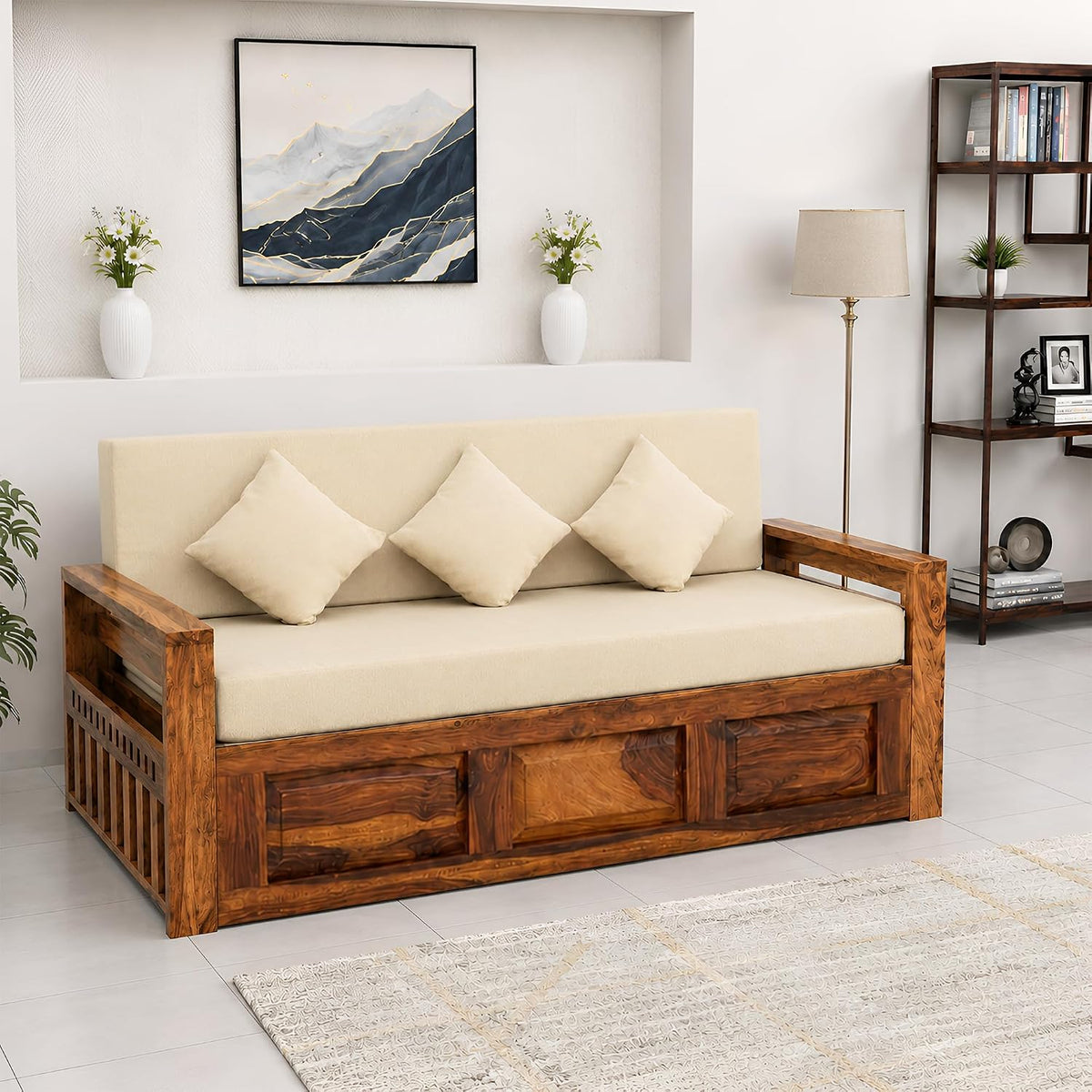 A sheesham wooden sofa bed with cream cushions and three matching pillows, styled in a bright, modern living room setting.