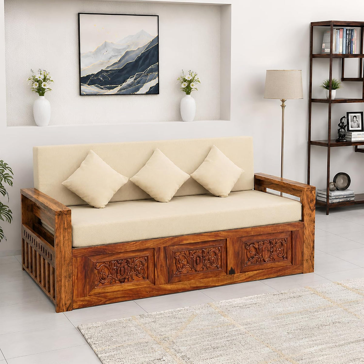 A sheesham wooden daybed with a carved brown frame and cream cushions, styled in a bright, modern living room setting.